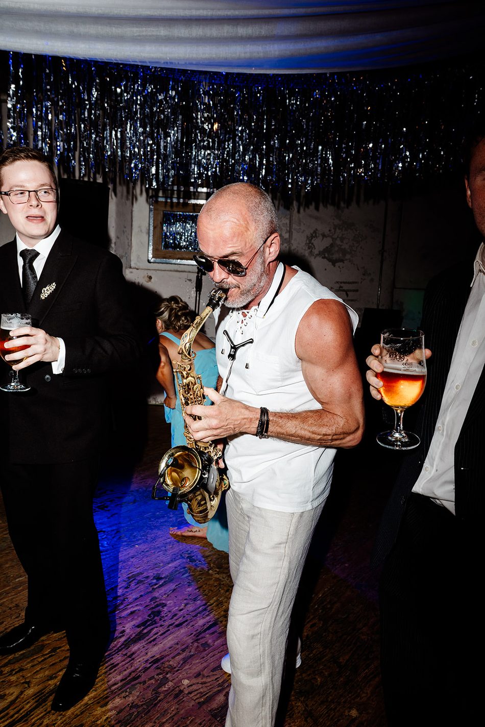 Paul Martyn playing saxophone among dancing wedding guests under tinsel decorations