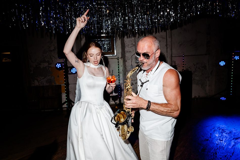 Bride dancing with a drink beside Paul Martyn playing saxophone at a wedding party