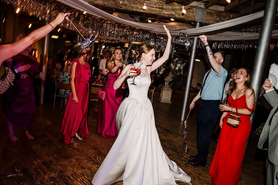 Bride in a white dress dancing as wedding guests celebrate around her